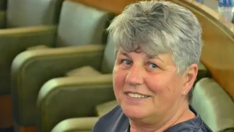 LDRS An image of Yvonne Gagen taken in the council chamber. She is looking at the camera and smiling. She has short grey hair and is wearing a navy top. She is sitting in a light green chair.