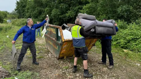 Double H Nurseries Two men are lifting a sofa into a skip while another man is putting waste in there from a different side.