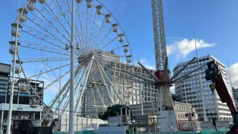 The of the City Star Flyer on Thursday. One man is in a hi-vis jacket. The ride can be seen cordoned off by a green fence with a big wheel in the background. 