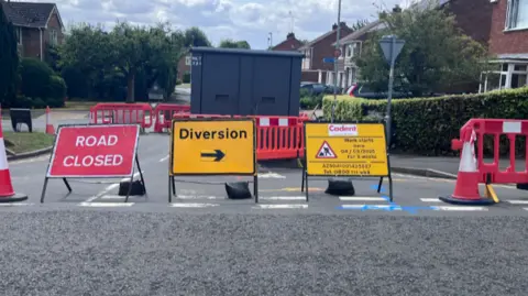 Roadworks signs and road closed signs are in front a a road that is closed in the town warning of diversions