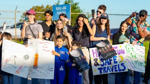 Getty Images Employees from the Johnson Space Center hold signs along Brantly Avenue near Ellington Field as they gather to send off the Artemis II astronauts ahead of their mission to the moon in Houston, Friday, March 27, 2026. 
