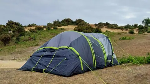 New Forest Police A large grey tend with bright green stripes and guide roles is pitched in the New Forest. It is surrounded by dry looking grass and vegetation.