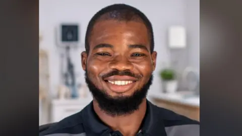 An AI-generated image of a man smiling. He is in a kitchen which is blurred in the background. He has a medium-length, dark beard and short dark hair. He's wearing a dark blue and grey polo shirt.