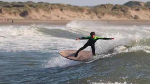 Neil Phillips Oscar in a black and green wetsuit surfing