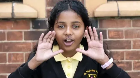 A young girl wearing school uniform has her hands by her face as if she is yelling