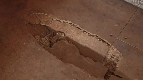 An image showing a visible depressed hole and cracks in what appears to be plywood, where Ms Lawson's foot has gone through the floor in her bedroom