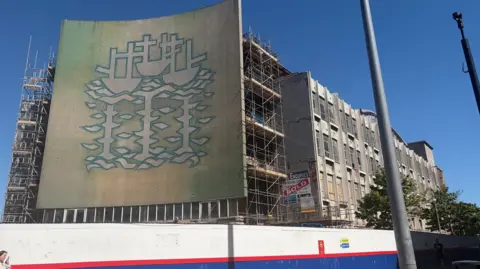 A giant mural depicting three ships covers the front of a former department store. 