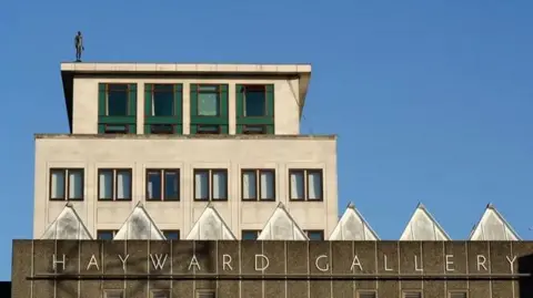 Southbank Centre A statue of a man is on top of a large concrete building with a sign on the front that reads "Hayward Gallery".