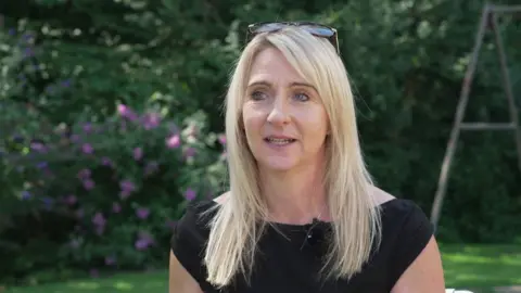 Cara Shardlow has long blonde hair and is wearing a black sleeveless top.