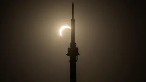 BBC Weather Watchers/Mac A partially covered sun lights up the dark sky. It can be seen from the silhouette of a large tower.