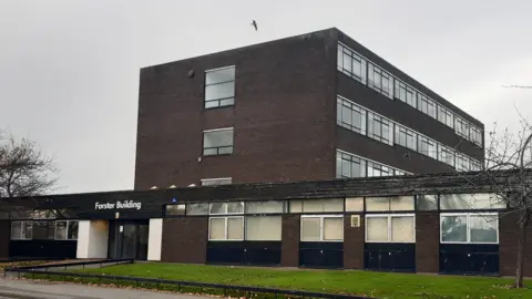 BBC A dark brick building with glass entrance doors. The name "Forster Building" is written above the entrance in white lettering.