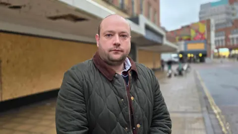 Paul Moseley/BBC Martin Schmierer is standing on a street. He's wearing a dark green padded coat and there is a neutral expression on his face.