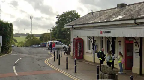 A Google Maps street view of the front of the train station in Liskeard, Cornwall. There are people stood at the entrance of the station.