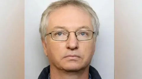 Avon and Somerset Police A custody picture of Chapman. He has no expression on his face, and wears dark, thin-framed glasses. 