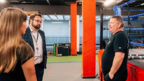 Cleveland PCC Matt Storey, who has a dark beard and glasses, speaks to a man from the boxing club next to a boxing ring