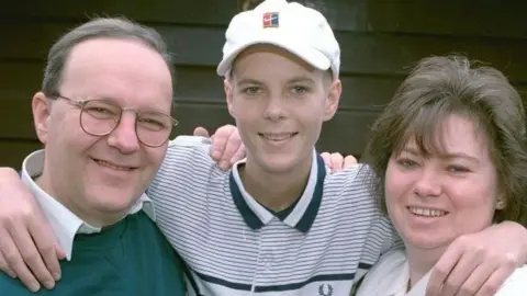 Lucas family An old picture of a young Christopher Lucas standing with his arms around his parents' necks