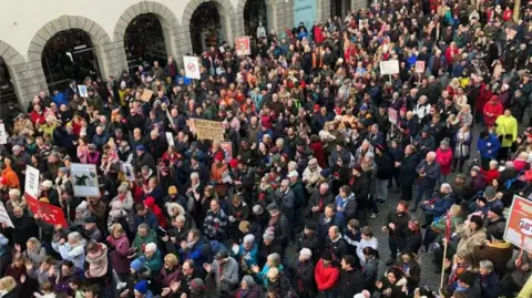A large crowd of people from above. They are holding various anti gst signs.