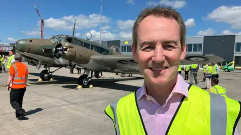 Charles Johnson, Head of Planning and Development at Leeds Bradford Airport, said the landing ensures the airport keeps in touch with its "rich aviation history" in a hi-vis jacket and a pink shirt standing in front of a plane on an airstrip.