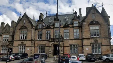 Google The High Court in Stirling, a brown brick building, with cars parked in front of it.