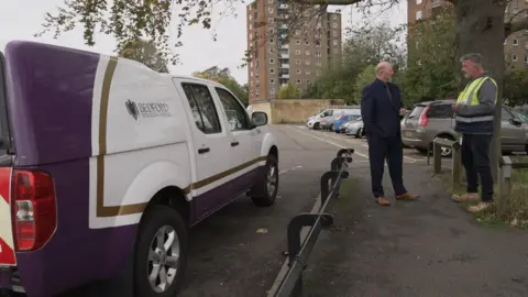 Shaun Whitmore/BBC A 4x4 van with Bedford Borough Council branding is parked in Bedford near some high rise flats