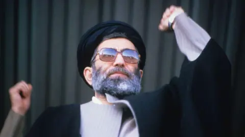 Hulton Archive via Getty Images Ayatollah Khamenei making a speech in 1986. He is holding his arm aloft 