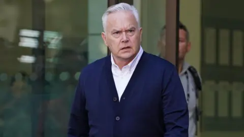 PA Media Huw Edwards in a blue cardigan walking out of court after his sentencing