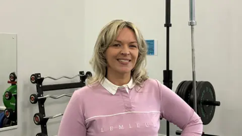 Steph Graham, Longtown Community Centre Manager, wearing a pink sweatshirt and standing in the community centre gym.