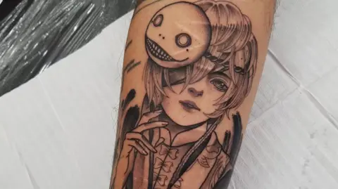 Löiz Dominguez Close-up of a black ink tattoo of an anime character. Self-inflicted scars are visible beneath the design 