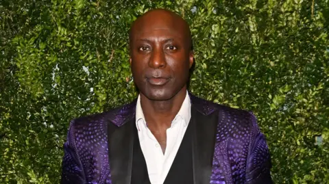 A heads-and-shoulder shot of Ozwald Boateng in a purple jacket in 2024