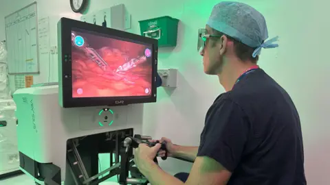 University Hospital Southampton Surgeon Ewan Brownlee operates the Versius robot, watching a patient's internal soft tissue on a screen as he manipulates hand-held controls