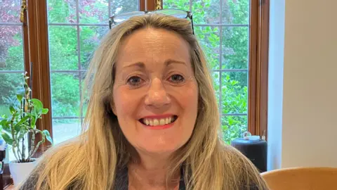 Guy Campbell/BBC The Reform UK candidate with blond hair sitting in front of a kitchen window 