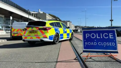 A police car parked on the promenade next to the Castle Mona shops in Douglas with a "Police Road Closed" sign to the right.