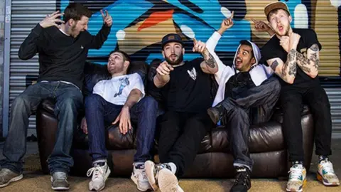 THE BEATBOX COLLECTIVE A group of five young men, dressed casually in hoodies, jeans, t-shirts, caps and trainers, sit together on a sofa, pointing their fingers in the air in celebration. On the end to the right is Rupert Oldridge, who recorded the sounds for the beatbox bins