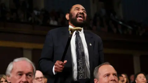 Man appears to yell while holding cane in the air