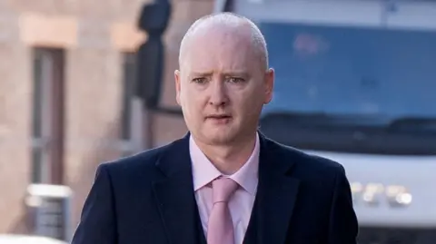Graeme Dott arriving at the High Court in Glasgow. He is wearing a dark suit over a pink shirt witha pink tie.