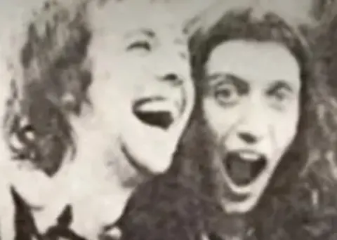 A black and white image of two men with long hair laughing with their mouths open