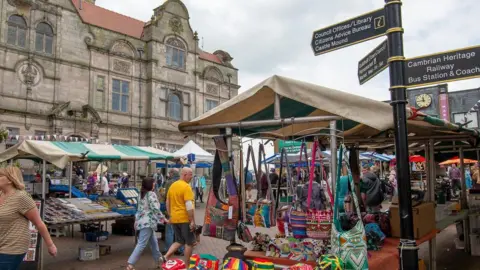 Oswestry's Guildhall, a three-storey building, is in the background. Market stalls and some people are in the foreground.