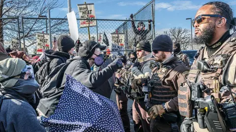 AFP via Getty Images Law enforcement officers standing in a line in front of protestors wearing gas masks