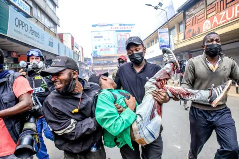 Getty Images Kijana mwenye hasira akimsaidia mwenzao aliyepigwa risasi wakati wa maandamano kuhusu mauaji ya polisi ya watu waliokuwa wakiandamana kupinga pendekezo la mswada wa fedha wa Kenya mjini Nairobi tarehe 2 Julai.