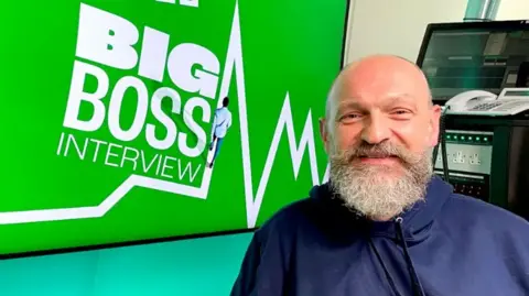 Chris O'Shea, boss of Centrica, in the BBC's Big Boss studio. He has a big bushy beard and is wearing a blue hoody.