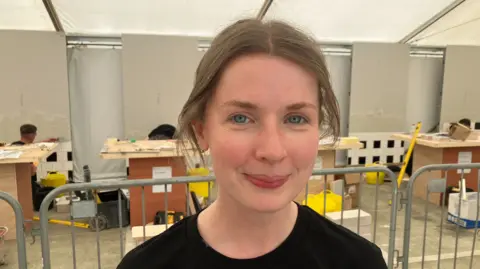 Rebecca Gavigan. She has brown hair tied back, blue eyes, wearing a black t shirt.