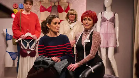 Sky UK Tina Fey and Emma Sidi, wearing a cropped red wig, in the changing rooms of a women's underwear shop 