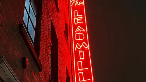 BBC/Oli Constable The side of a red brick building with a huge red neon sign 