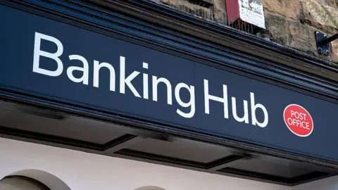 A close-up shot of a blue banking hub sign. The words "Banking Hub" are written in white, with a red Post Office logo next to them. 