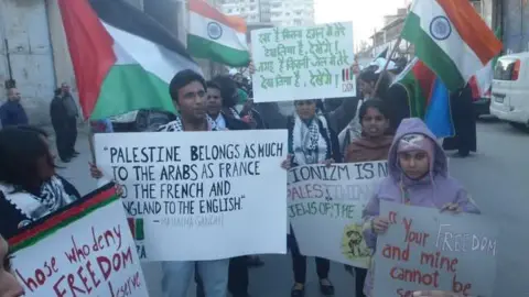 Suri went to Gaza with an international humanitarian convoy in 2010. He is seen with a group of people holding posters, with flags of India and Palestine in the background.