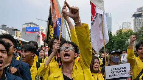 An Indonesian student protester wearing yellow marching on the street in Jakarta with one arm raised