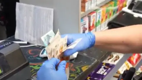 Sussex Police A close up of an officer's hands wearing blue latex gloves counting paper cash.