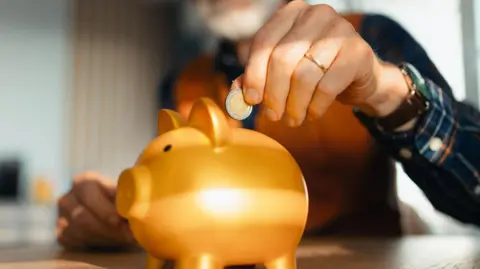 Getty Images Un hombre coloca una moneda de euro en una alcancía de oro. 