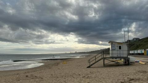 CDark and cloudy sky looming over a sandy beach with beach huts in the distance