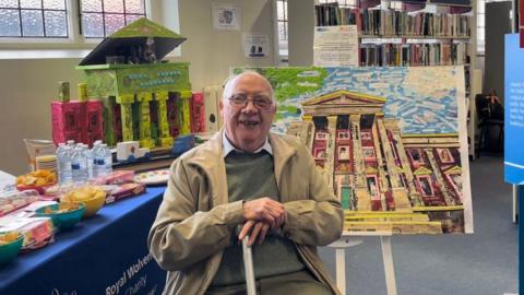 An elderly gentleman sitting in front of a model of the Wolverhampton Royal Hospital
